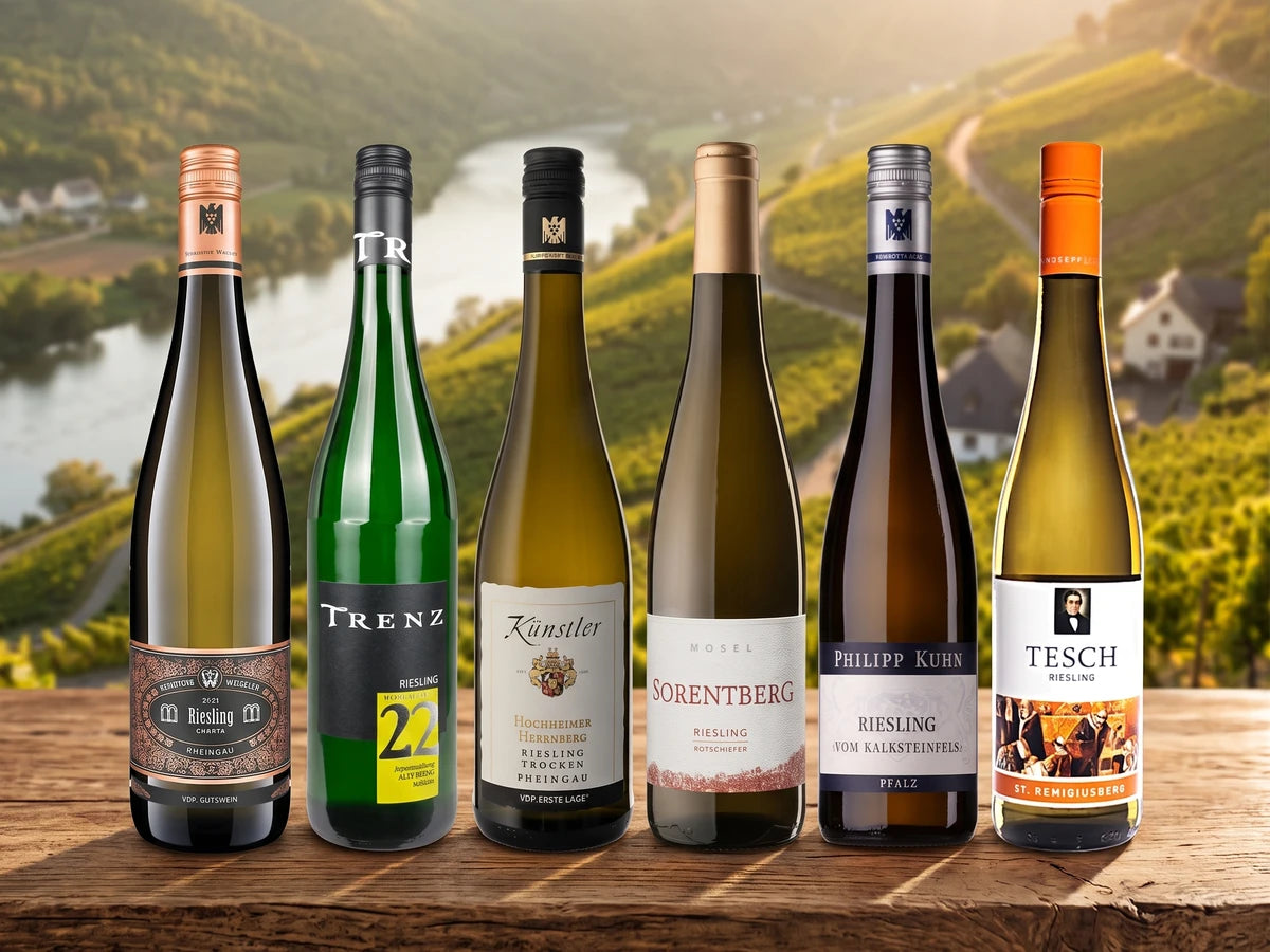 Probierpaket Riesling – sechs Flaschen deutscher Riesling auf einem Holztisch vor Steillagen-Weinbergen an einem Flusstal.